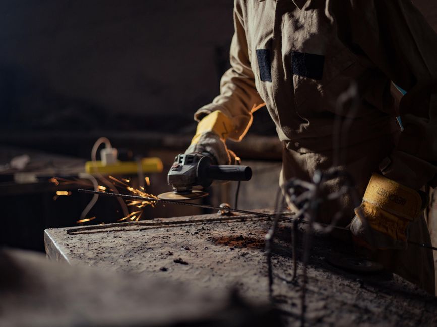 A worker in protective gear using an angle grinder in a dimly lit industrial workshop.